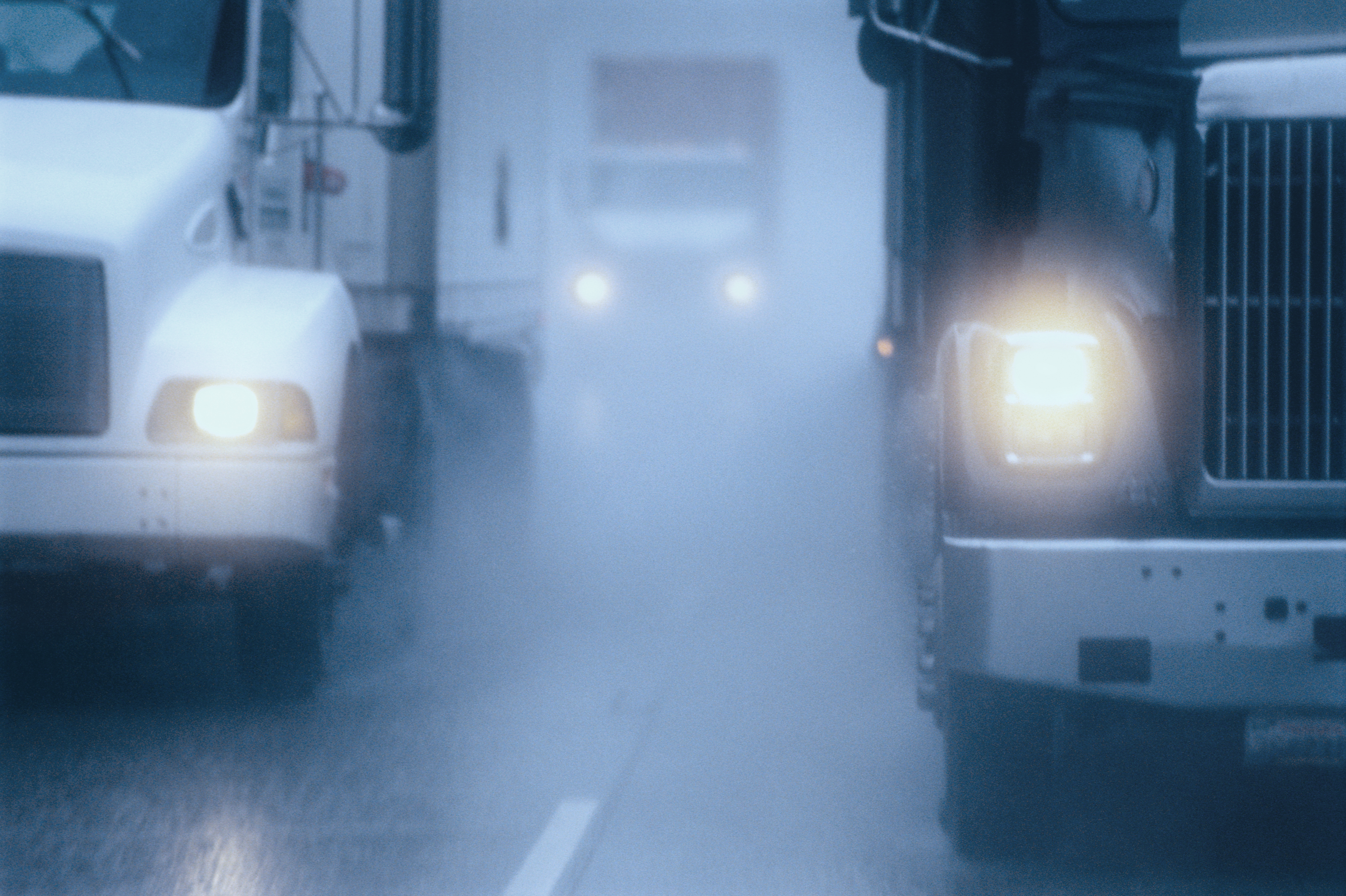 Large commercial delivery trucks navigating hazardous road conditions during heavy fog and rain with headlights illuminated.